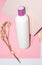 White bottle for shampoo and cosmetics with place to write and logos on pink background with plaster and flower.