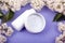 White bottles with cosmetics for skin care with white lilac flowers on the violet background close-up. beauty, wrinkle prevention