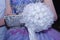 White bouquet of artificial flowers, a bag and a fragment of lilac dresses
