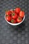 White bowl filled with small fresh tomatoes on grey background