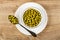 White bowl with green peas, spoon with green peas in plate on wooden table. Top view