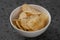 White bowl with organic potato chips sprinkled with fresh ground black pepper on concrete background