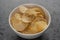 White bowl with organic potato chips sprinkled with fresh ground black pepper on concrete background