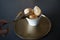 White bowl with sweet bites on a bronze tray and a woman hand using serving tongs to take one of them