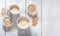 White bowls with oat seeds and flakes and  white mugs with oat milk on white wooden background.