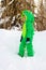 White boy in a green Dragon snowsuit standing on a snowbank