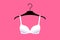 White brassiere is on hanger over bright pink background