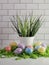 White bucket filled with green grass for spring surrounded by a bed of green paper shreds and shimmery Easter eggs in yellow, blue