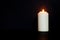 white burning candle on black background. burns in darkness, copy space. eternal memory, mourning,