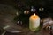 white burning candle for christmas and new year with decoration, spruce twigs, baubles and a golden ribbon on a rustic wooden tab