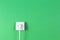 White cable plugged into electrical socket on green color background