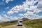 White camper driving on two lane highway with low southern Colorado mountains and scrubland in background