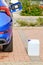 A white canister with a diesel exhaust fluid DEF for reduction of air pollution standing near a blue car.