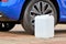 A white canister with a diesel exhaust fluid DEF for reduction of air pollution standing near a blue car.