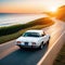 A white car drives off into the sunset along the road to the ocean