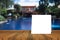 White card put on wood table and beautiful view of swiming pool at resort in background. product display template.