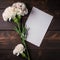 White carnation flowers with blank card on wooden background, top view