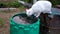 A white cat drinks water from a green barrel in the garden