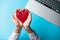 white caucasian female hands holding heart shaped toy near laptop on the wonderful blue background