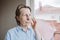 A white Caucasian woman puts cream on her face by the window