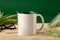 White ceramic mug, coarse sea salt scattered from bottle on wooden desktop, glasses and blooming spikelets on green