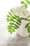 White ceramic pot with white blooming branch of rowan on linen patterned tablecloth.