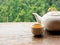 White ceramic teapot with hot tea water in small cup preparing on wooden table on natural green mountain view.