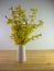 White ceramic vase full of fresh cut forsythia branches in the spring sitting on a real wood surface.  Yellow wildflowers brought