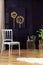 White chair against the wall with black and gold poster in living room interior with plants. Real photo