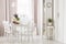 White chairs at dining table with plants in modern flat interior with pink drapes and window. Real photo