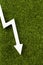 White chart arrow on green grass pointing down. Business loss symbol, ecology concept, green energy spending.