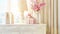 a white chest of drawers adorned with a bottle of pink flowers, a stylish lamp, and gift bags and boxes with delicate