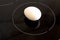 White chicken egg on black cooktop with circle