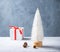 White Christmas toy fir tree on a wooden stand with white present box and cones  on a white table