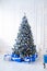 White christmas tree on white, decorated with blue ornaments and garland, lots of presents under the tree