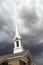 White Church Steeple Tower Below Ominous Stormy Thunderstorm Clouds.