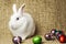 White clean beautiful Easter bunny next to a wicker basket with eggs in the background krashenyymi natural burlap cloth