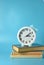 White clock with a bow on a stack of books on a blue background.