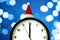 The white clock in red sunta hat shows five to seconds midnight, on the blurry background. Countdown to the new year