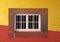 White closed wooden house window in a stone frame on a brightly painted red and yellow wall in typical portuguese colors