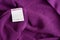 White clothing label with care information on purple garment, top view