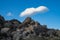 White cloud in blue sky above rocky wilderness hill