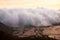 White cloud of mist entering and covering a rice field landscape in a valley between mountains at sunset.