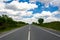 White clouds on blue sky above a highway. Green grass and trees beside highway