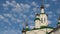 White clouds move against a bright blue sky, towers and domes of an Orthodox