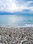 White clouds over the water and a pebbly shore