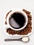 White coffee cup with coffee, plate with coffee beans and black teaspoon with sugar