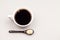 White coffee cup with coffee, plate with coffee beans and black teaspoon with sugar