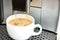 White coffee cup is stand in coffee machine with cappuccino device. Fragrant espresso is pouring into the mug. Morning coffee.