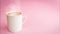 White colored cup with hot cappuccino coffee coming out of smoke steam on a light pink background.